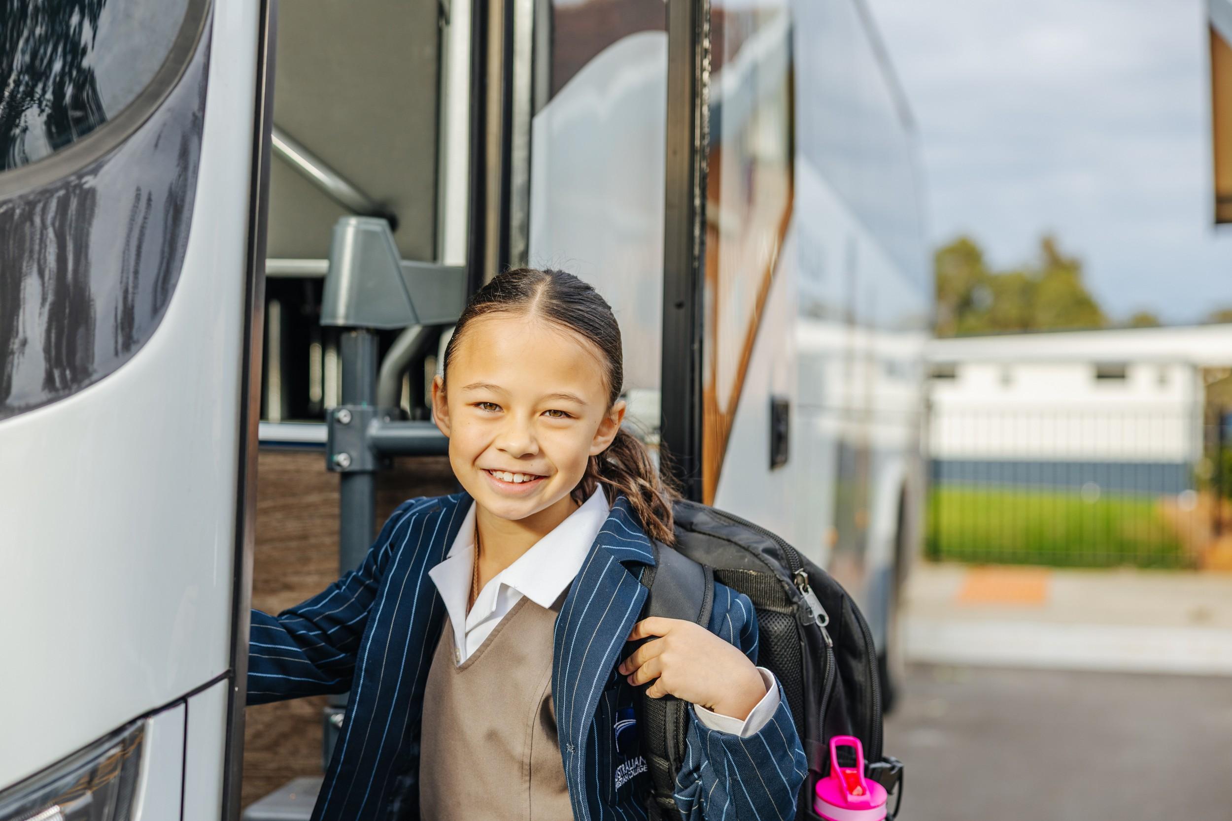 Smiling ACC Darling Downs student in uniform with backpack boarding the school bus