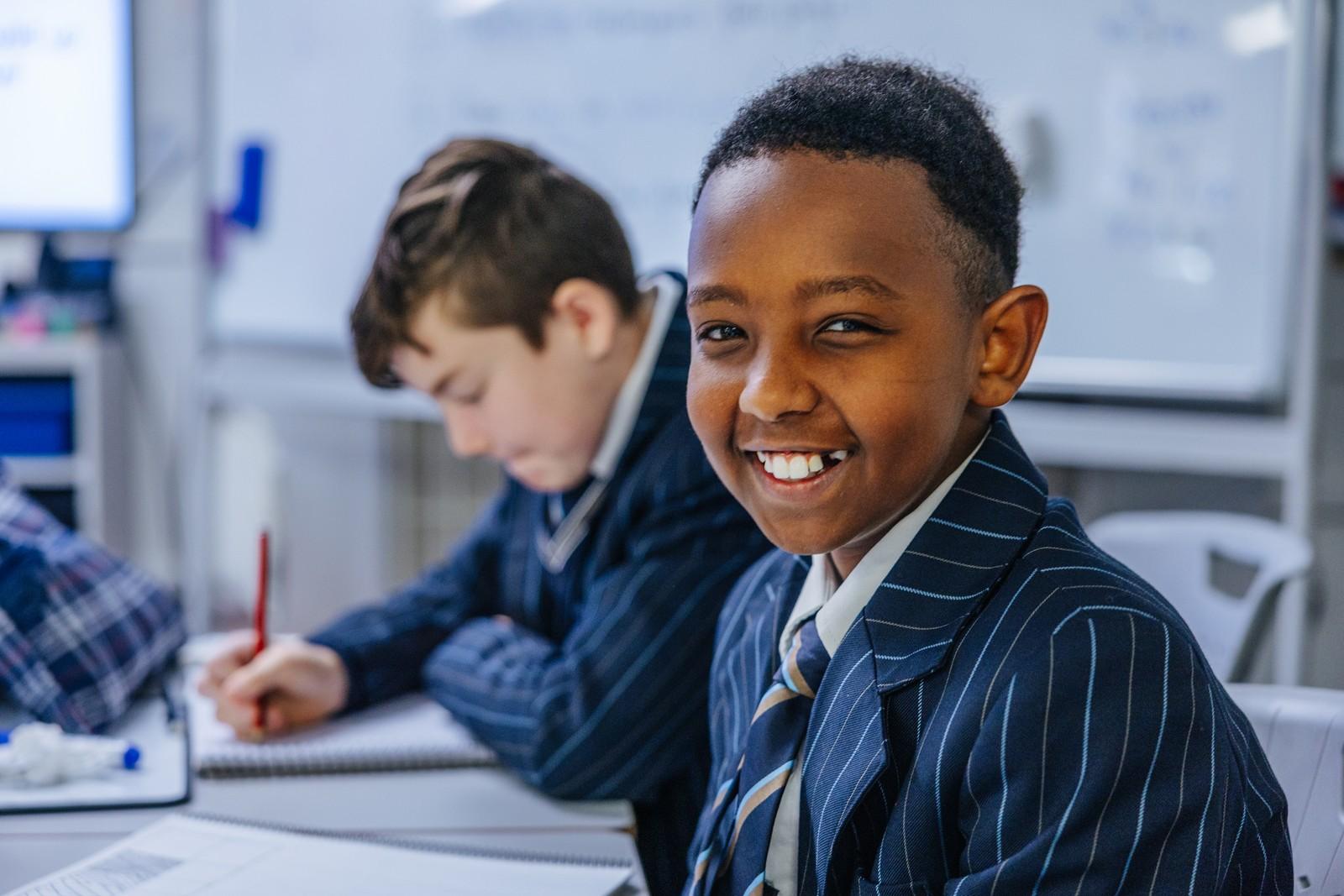 Smiling student in school uniform beside a classmate writing in a classroom at Darling Downs.