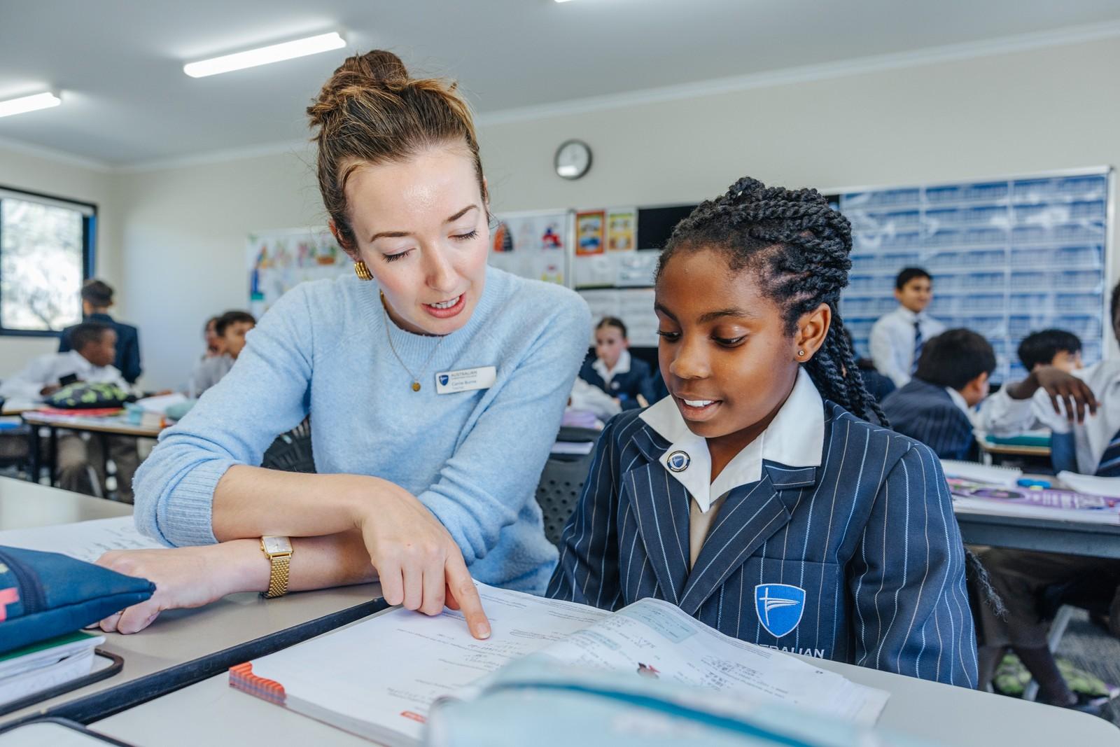 Teacher at Darling Downs helping a primary student work through a worksheet at a classroom desk.