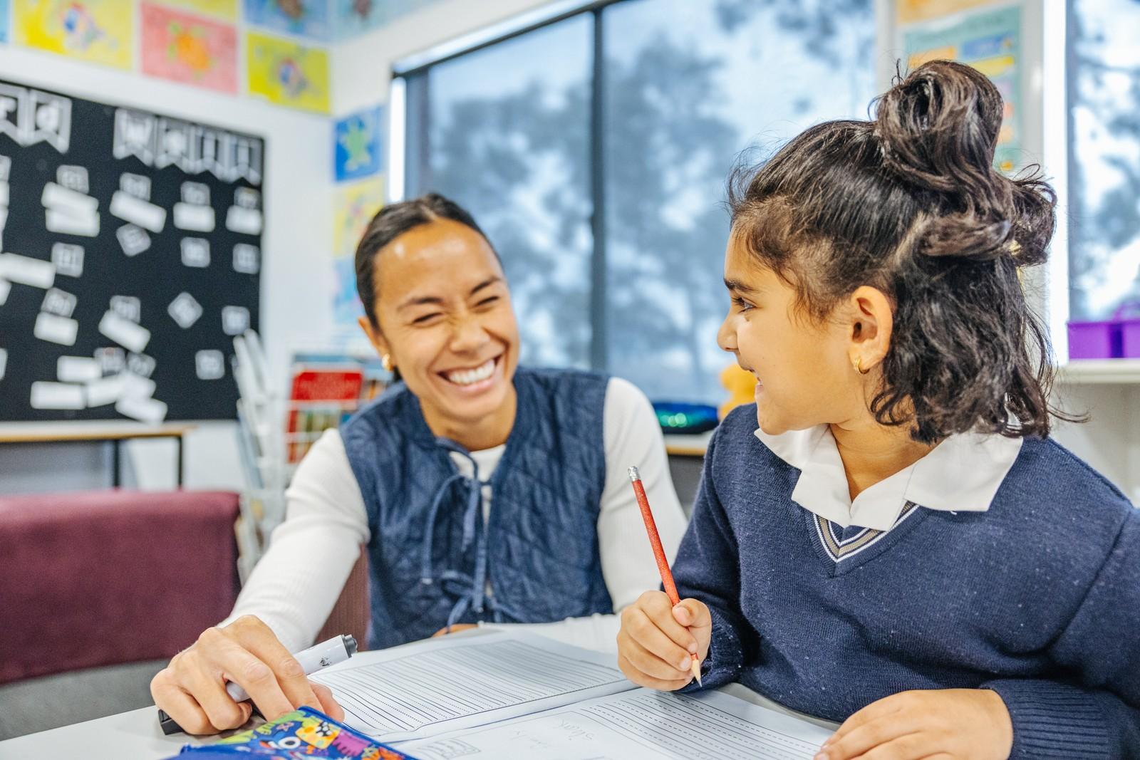 Teacher laughing with a student during deskwork, showing positive teacher-student relationships in a Christian classroom.