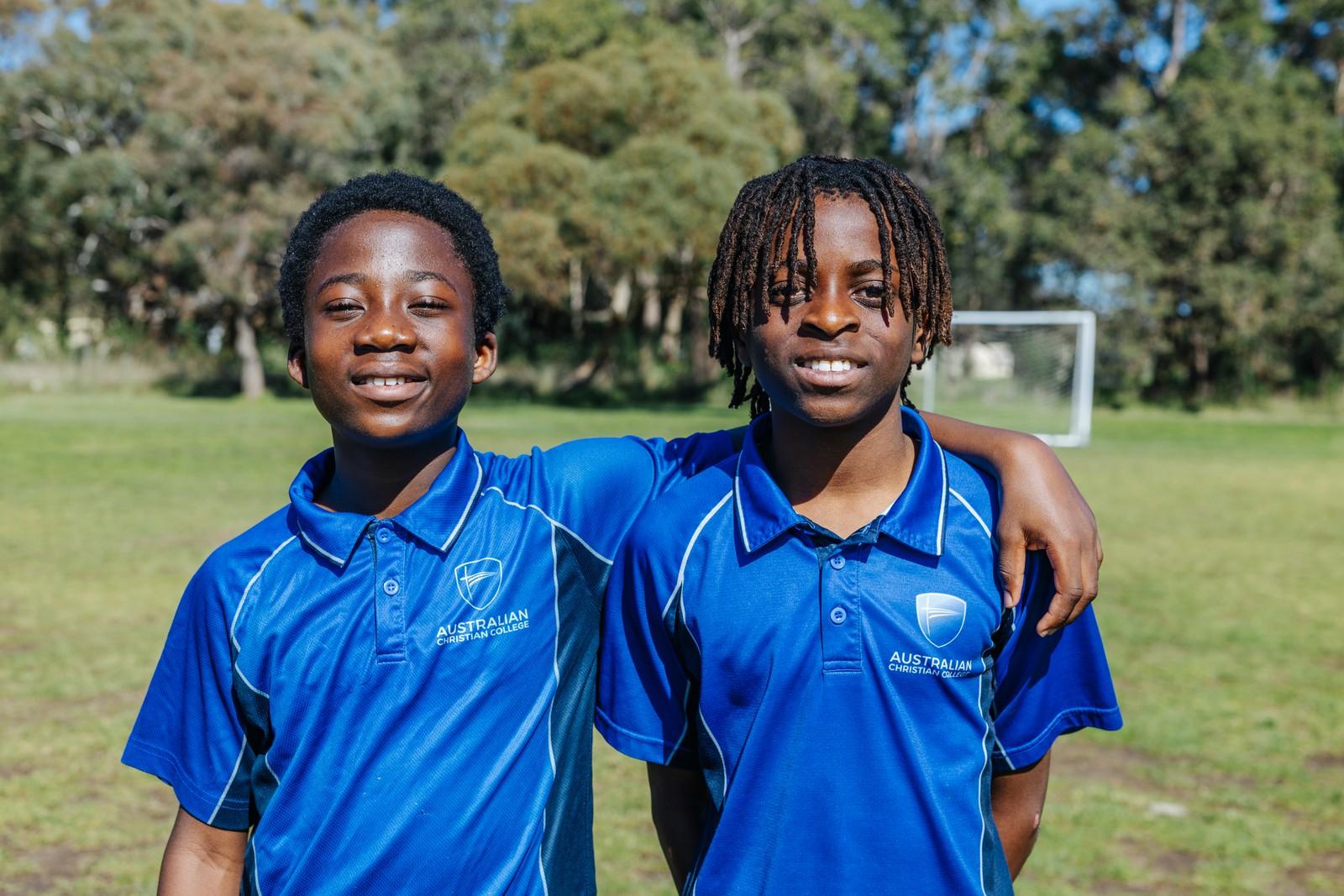 Two secondary students stand arm in arm and smile on the oval at Darling Downs, comfortable in a caring community.
