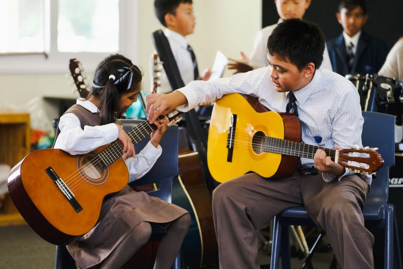 Male and female students sitting together learning guitar