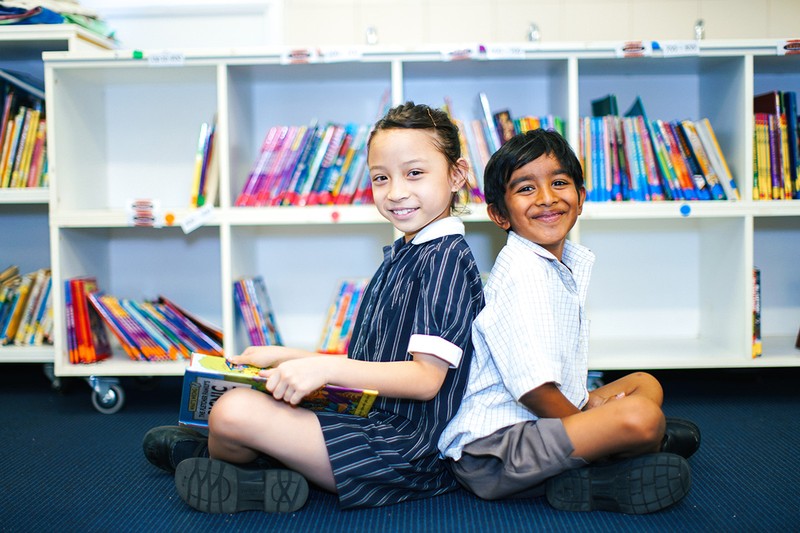 Primary aged boy and girl in uniform sitting back to back