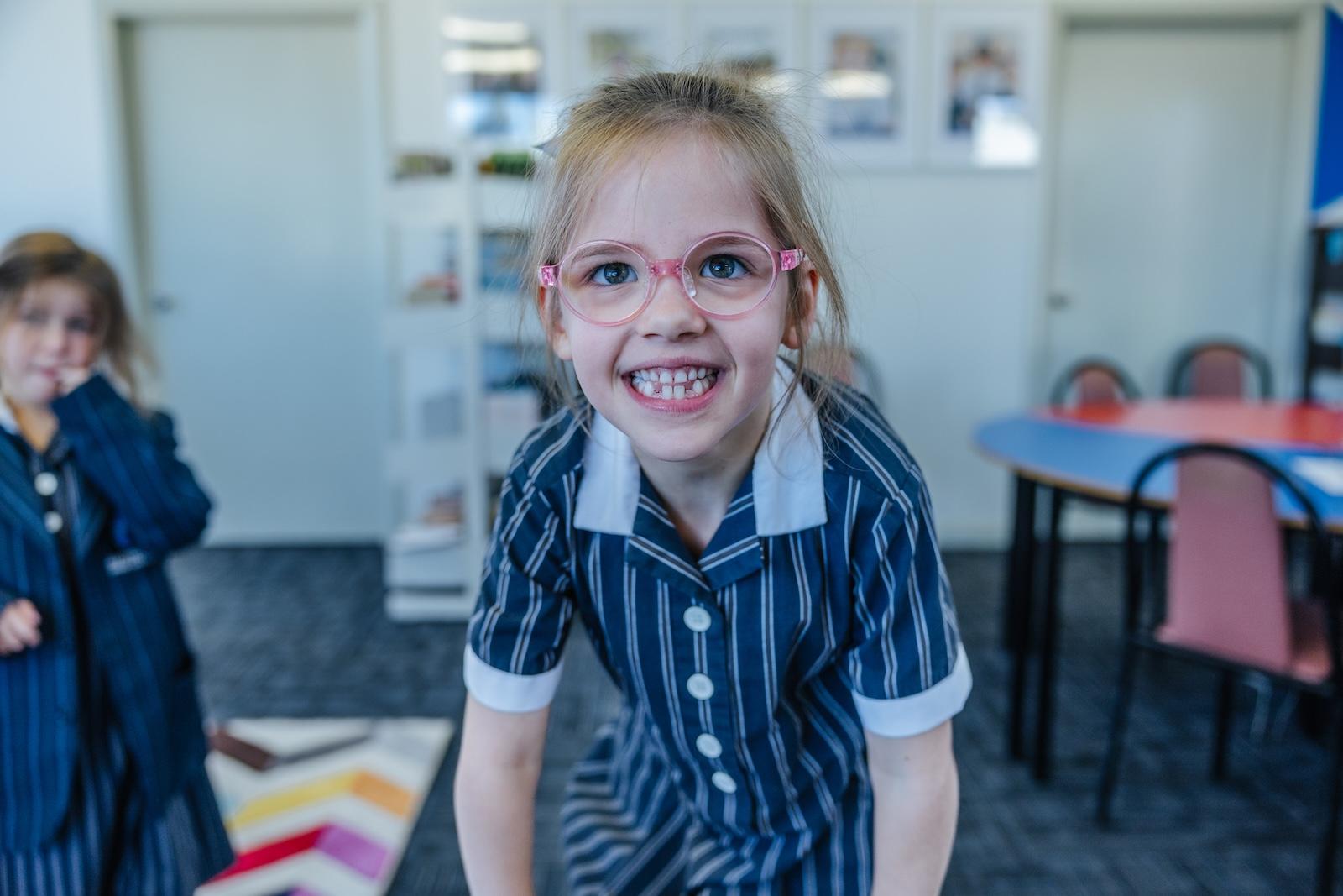 A young girl stands front and centre in her striped uniform, eyes bright behind pink glasses—confident in a space where care is part of the daily routine at ACC Echuca.