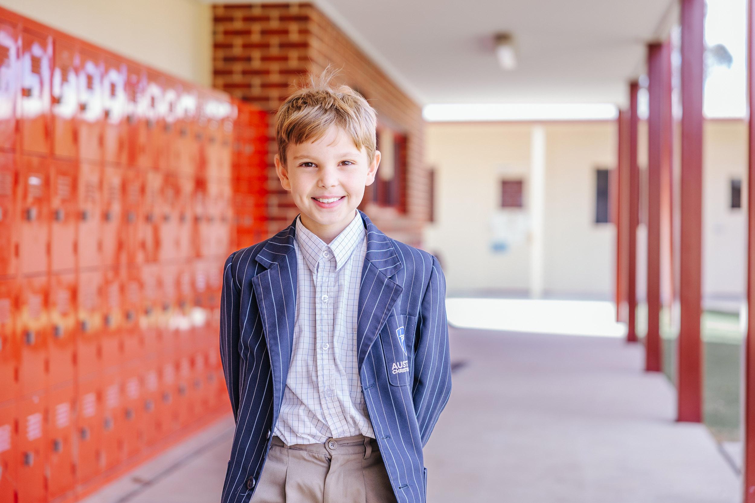 Confident primary student in ACC Echuca blazer smiling in front of orange lockers during a school tour moment