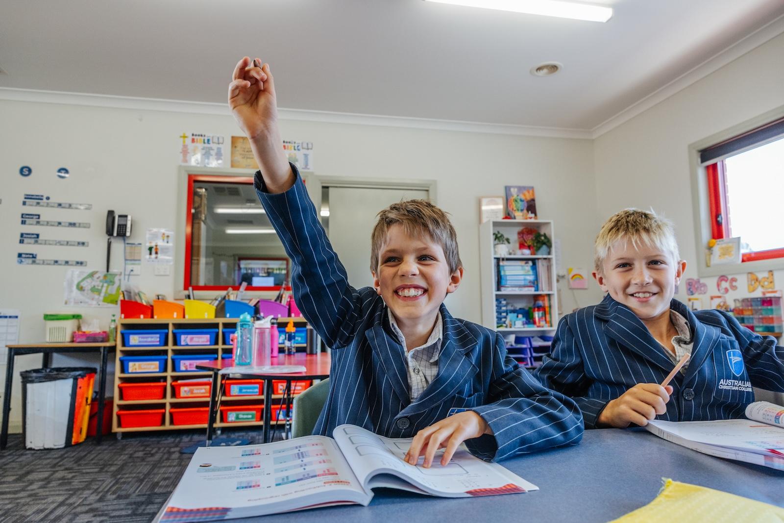 In a vibrant classroom, a student beams while raising his hand during a numeracy lesson—showing the confidence that comes from being encouraged to think, question, and participate at ACC Echuca.