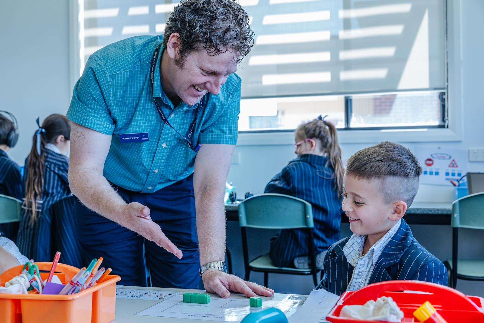 A teacher models a maths concept using cubes while a young student follows with focus—an example of Explicit Direct Instruction in practice at ACC Echuca.