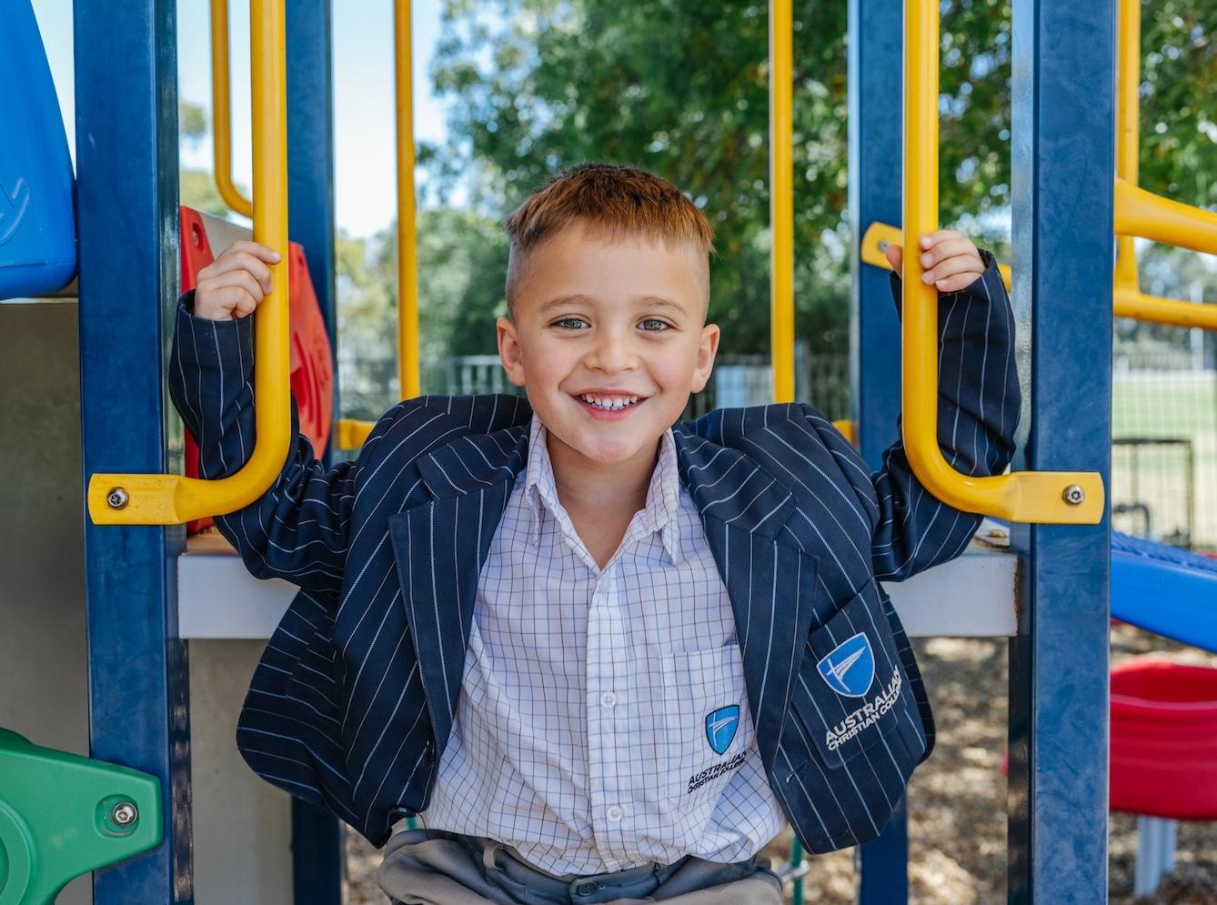 Happy young boy in Australian Christian College uniform on playground equipment, enjoying joyful learning and affordable private education.