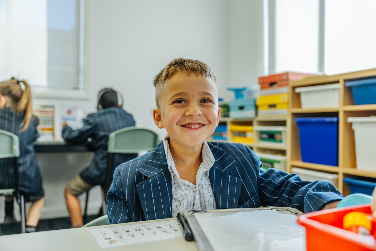 A young student in pinstripes beams from his desk as classmates focus nearby, capturing the energy of a welcoming ACC Echuca classroom.