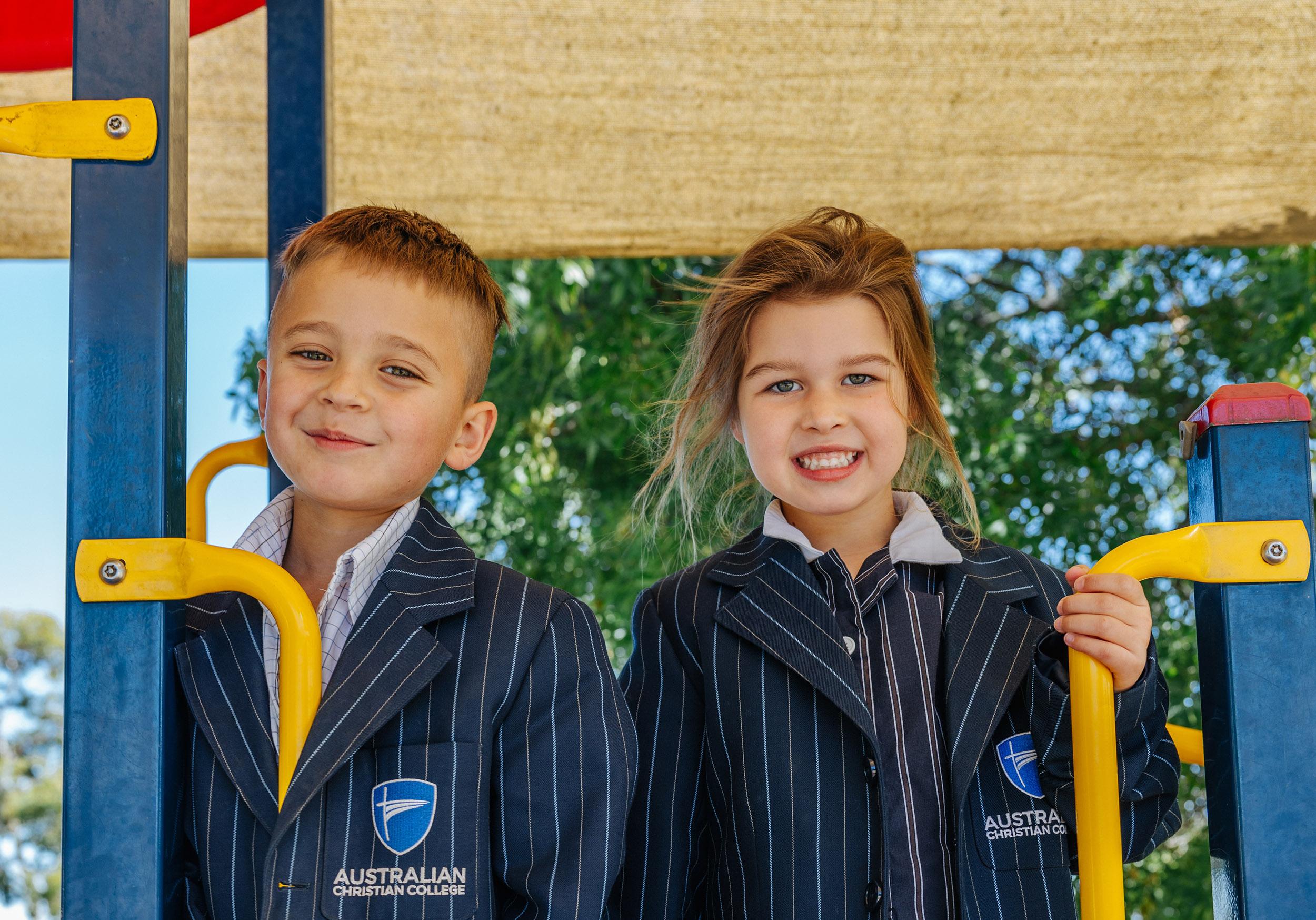 Two primary students smile at the top of the playground equipment, capturing the confident start and joyful energy of early years at ACC Echuca.