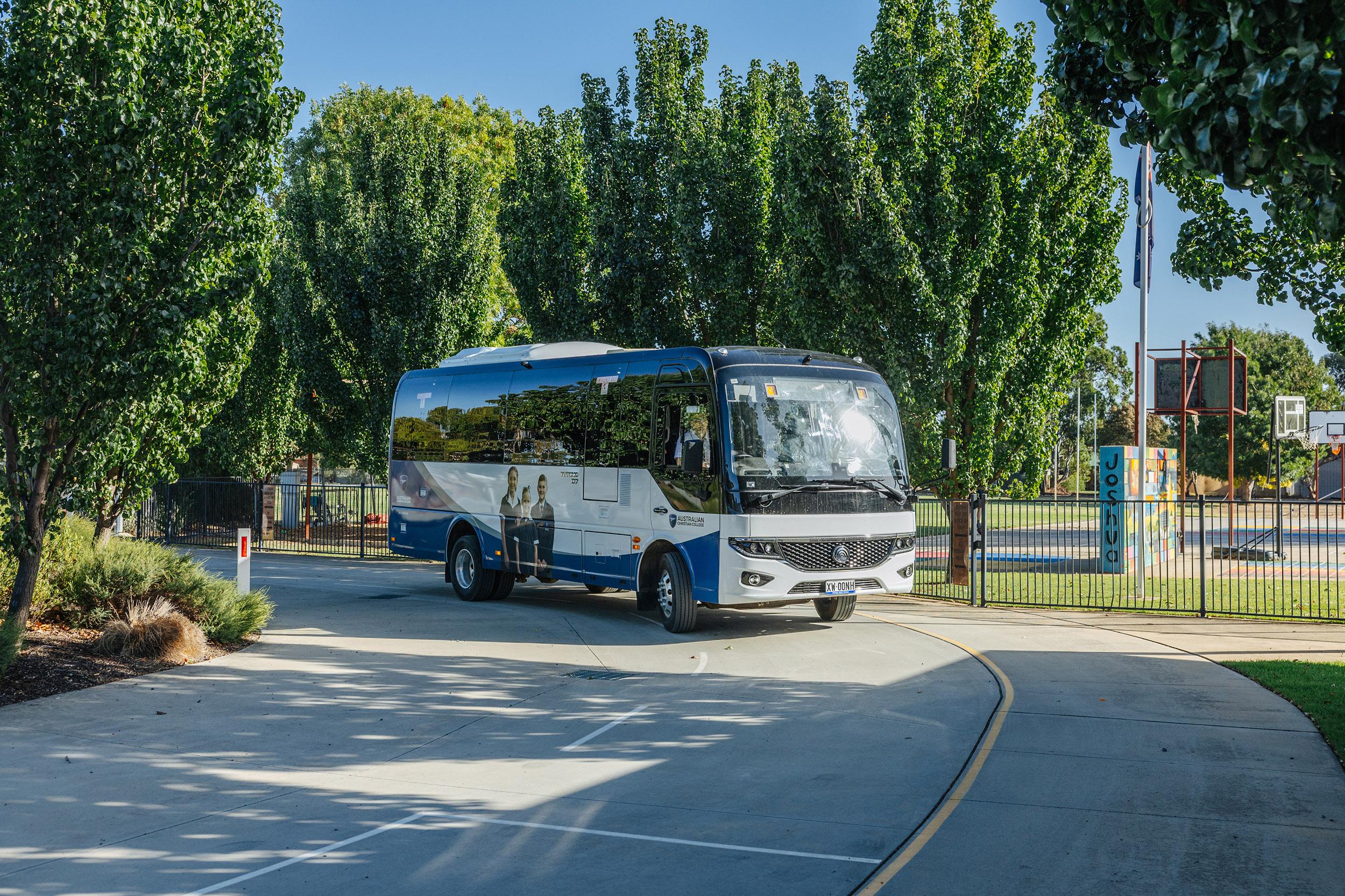 ACC Echuca school bus arriving on campus driveway beside basketball courts and leafy trees in regional Victoria