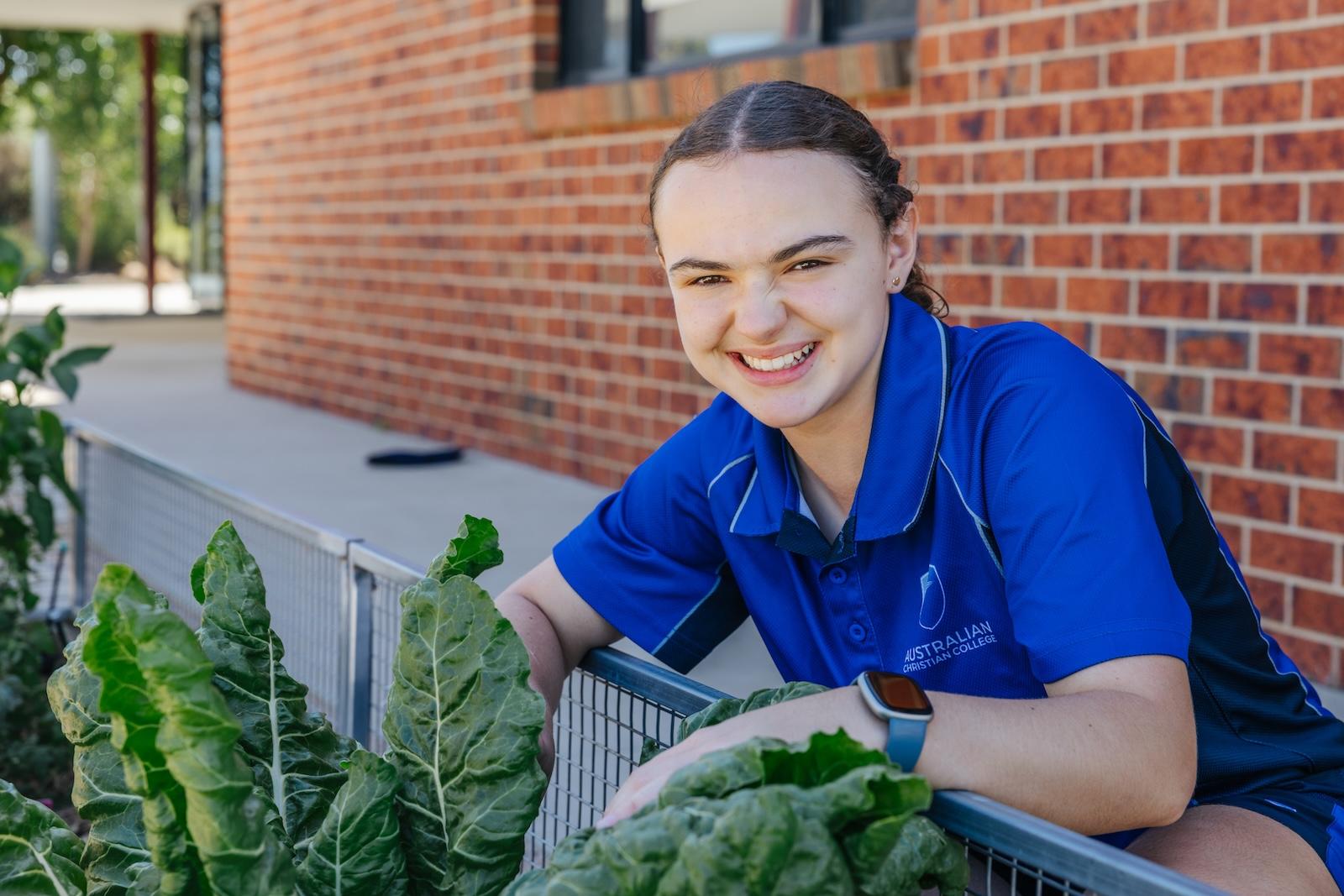 A student tends the school garden outside the brick building—hands in the soil, focus on more than just academics at ACC Echuca.