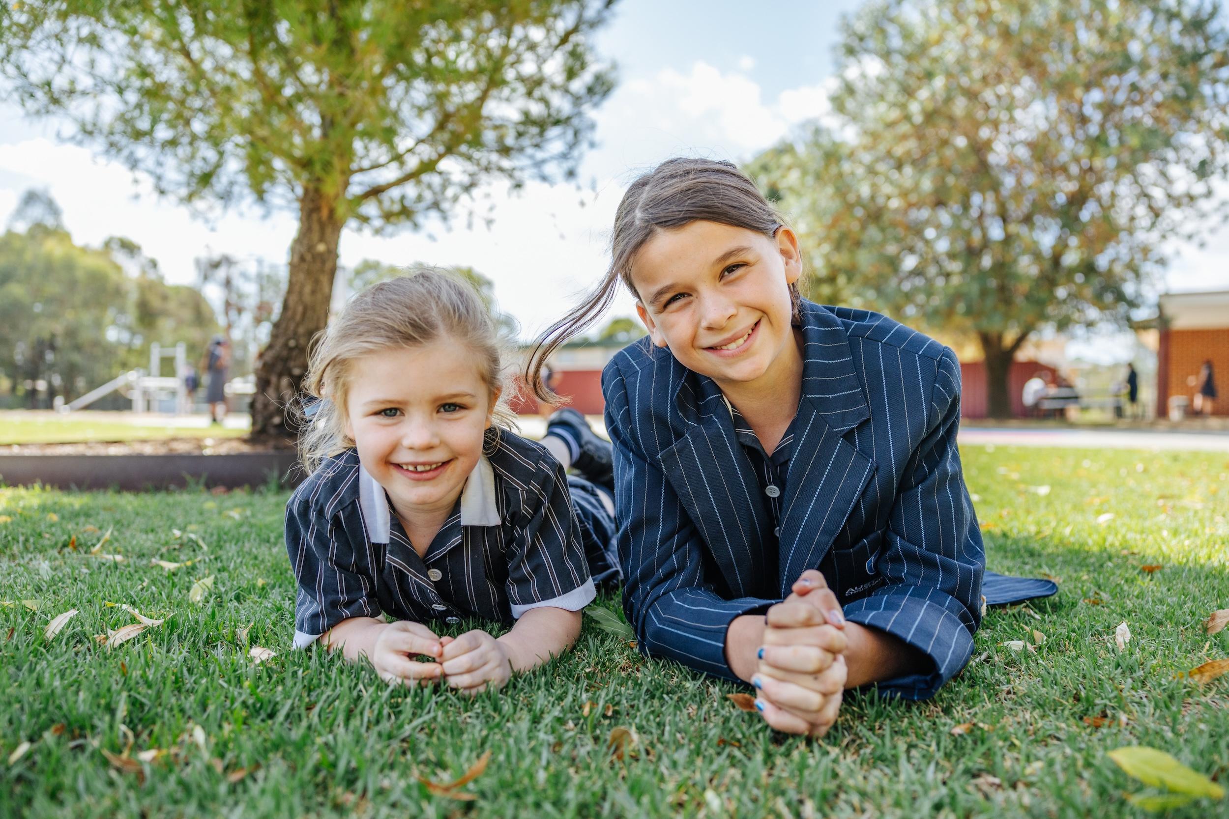 Sprawled across sunlit grass in their striped uniforms, two ACC Echuca students relax between classes—comfortable, connected, and confidently themselves.