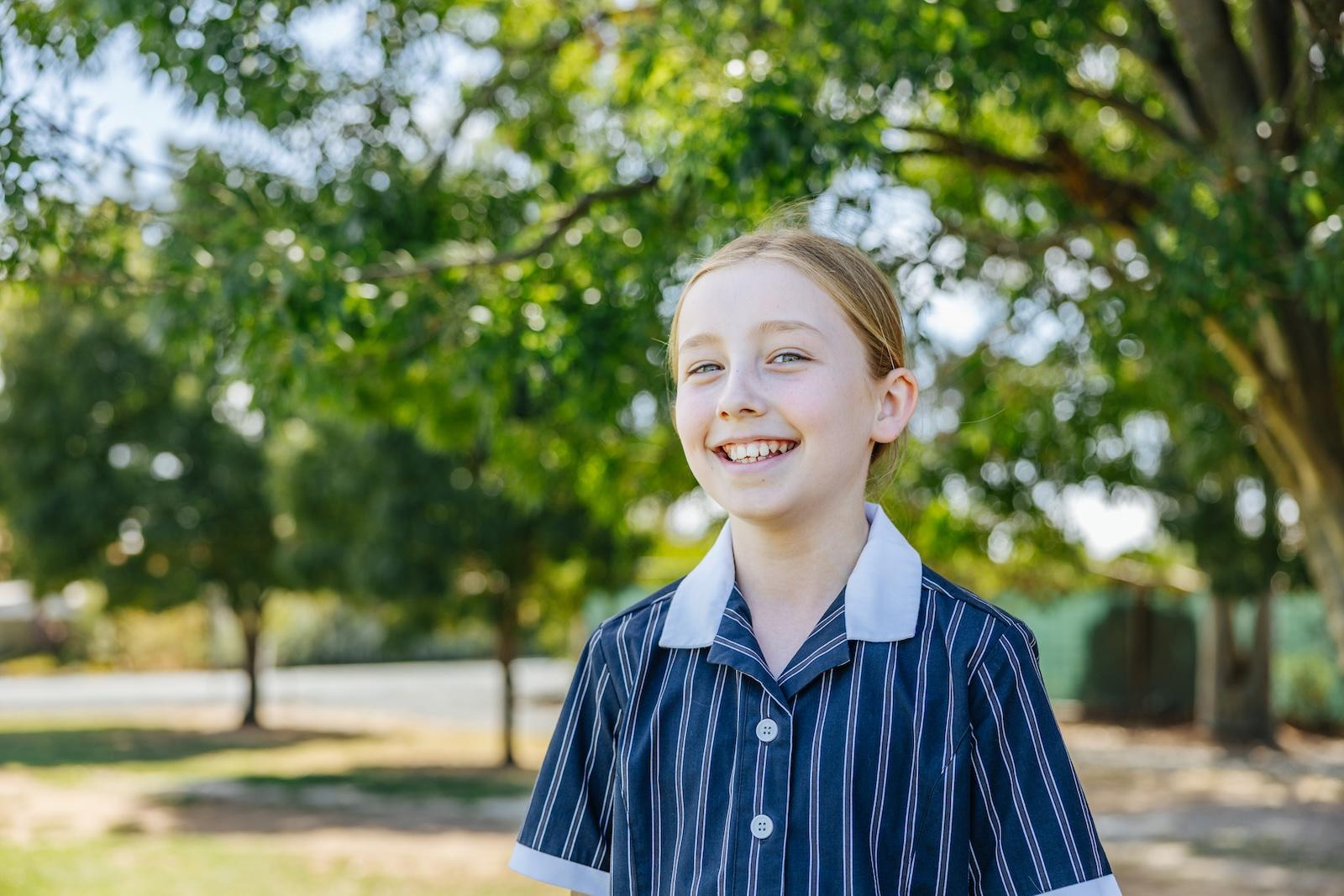 Smiling student in ACC Echuca uniform standing outdoors under leafy trees on a sunny school day