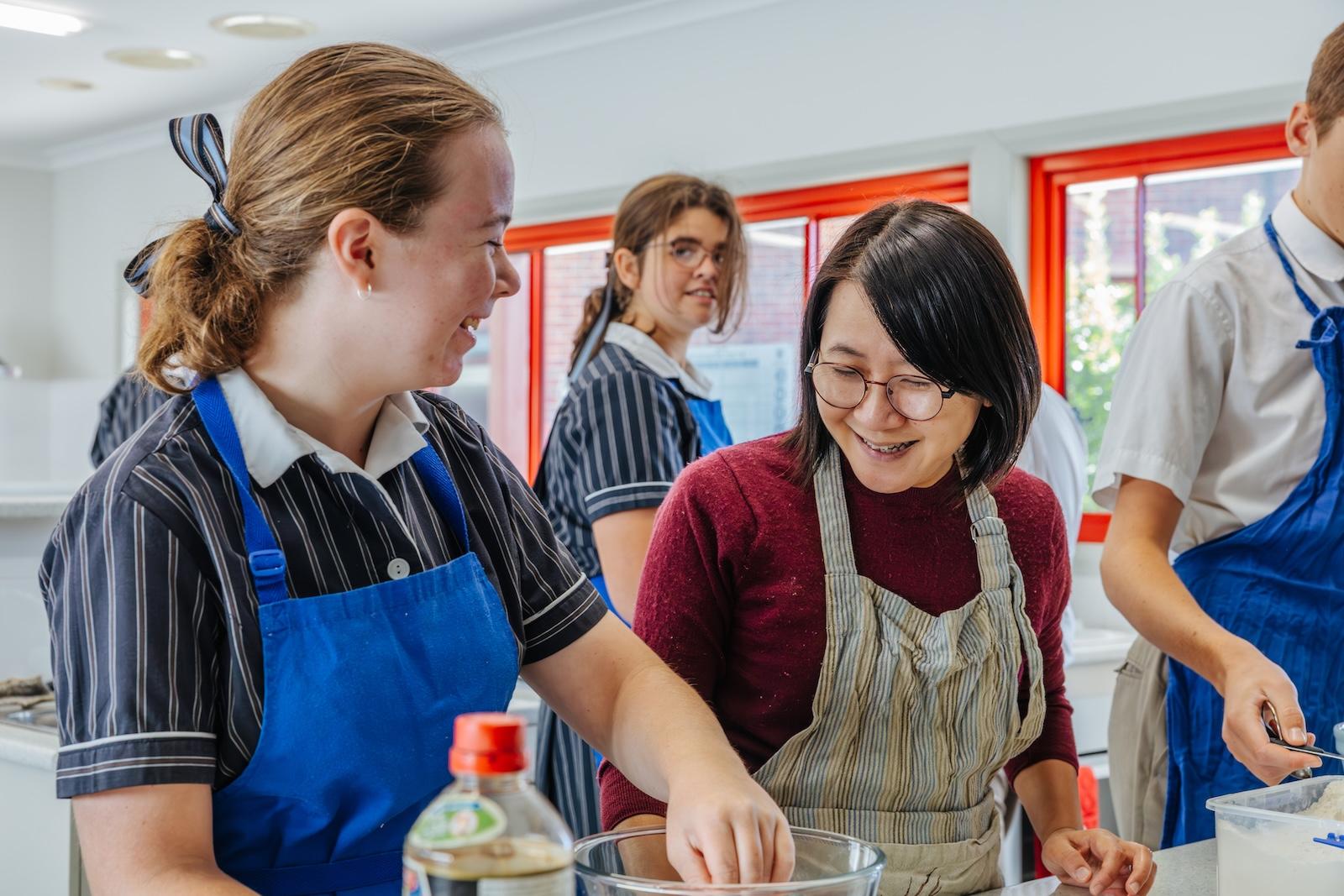 In the kitchen classroom, a student and teacher prepare ingredients side by side—focused, relaxed, and building trust through shared experience.
