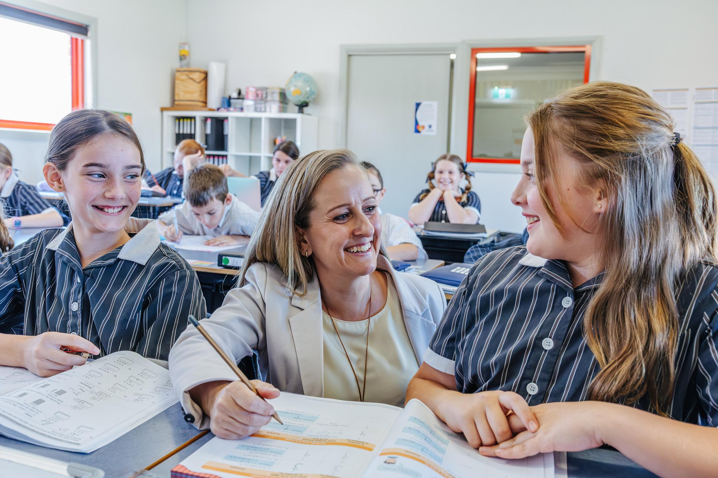 During a maths lesson, a teacher works closely with students, fostering understanding and confidence through structured, relational teaching at ACC Echuca.