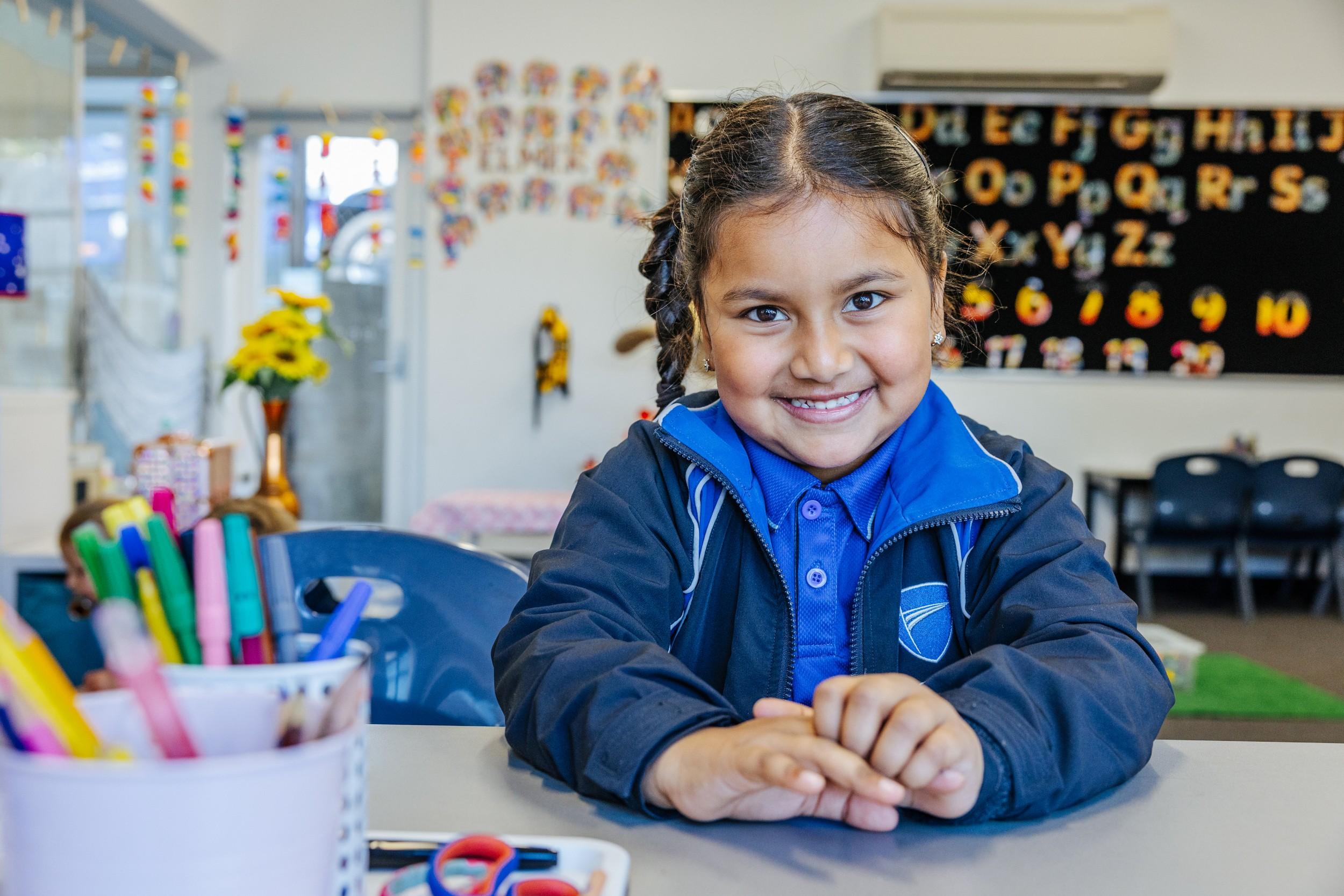 A primary student at ACC Hobart smiles at her desk in a colourful classroom