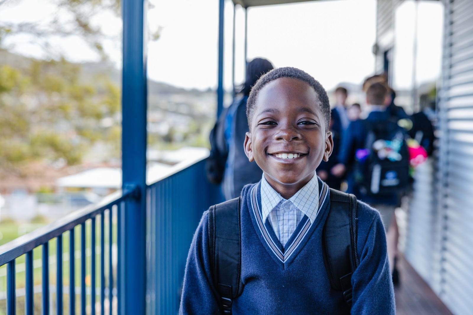 Primary student smiling in school uniform on the Geilston Bay campus walkway.