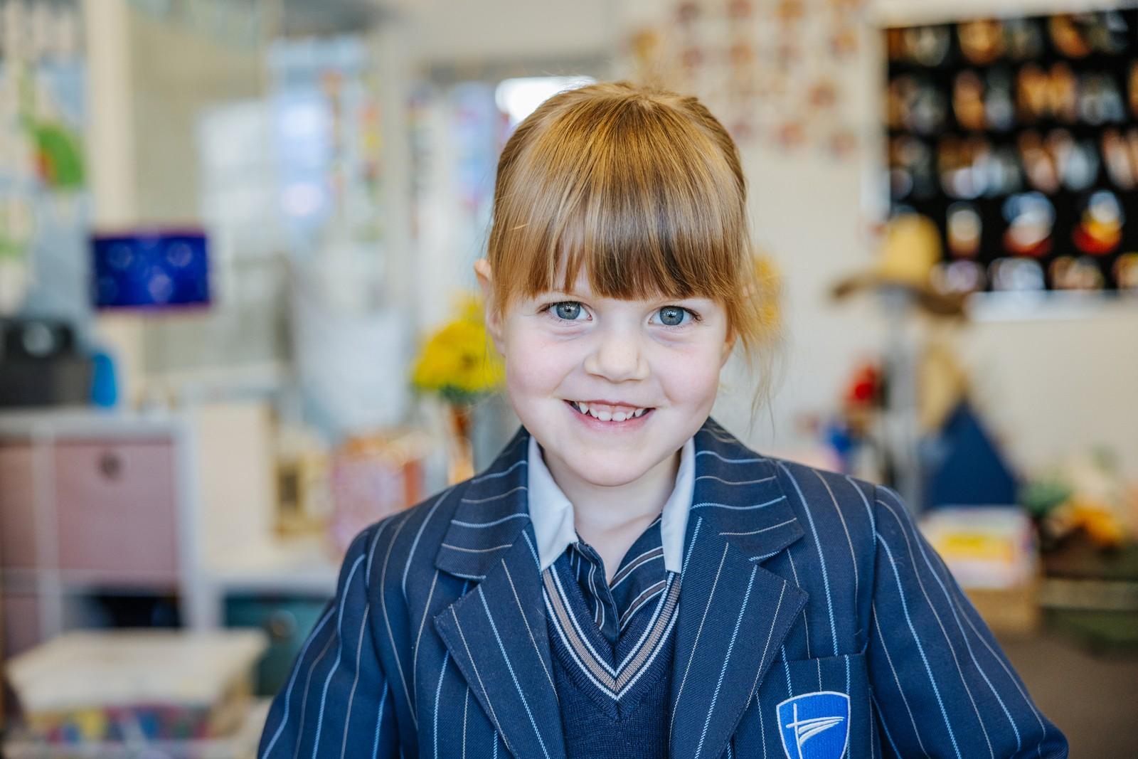 A young primary student in school uniform smiles warmly in a bright Geilston Bay classroom