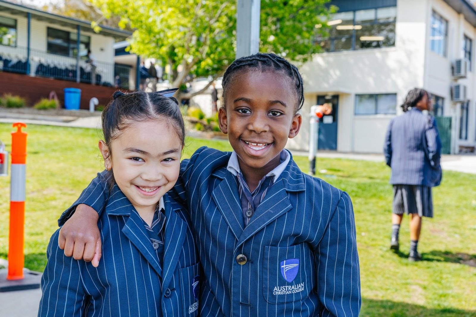 Two Geilston Bay primary students embrace and smile, showing genuine care in the schoolyard