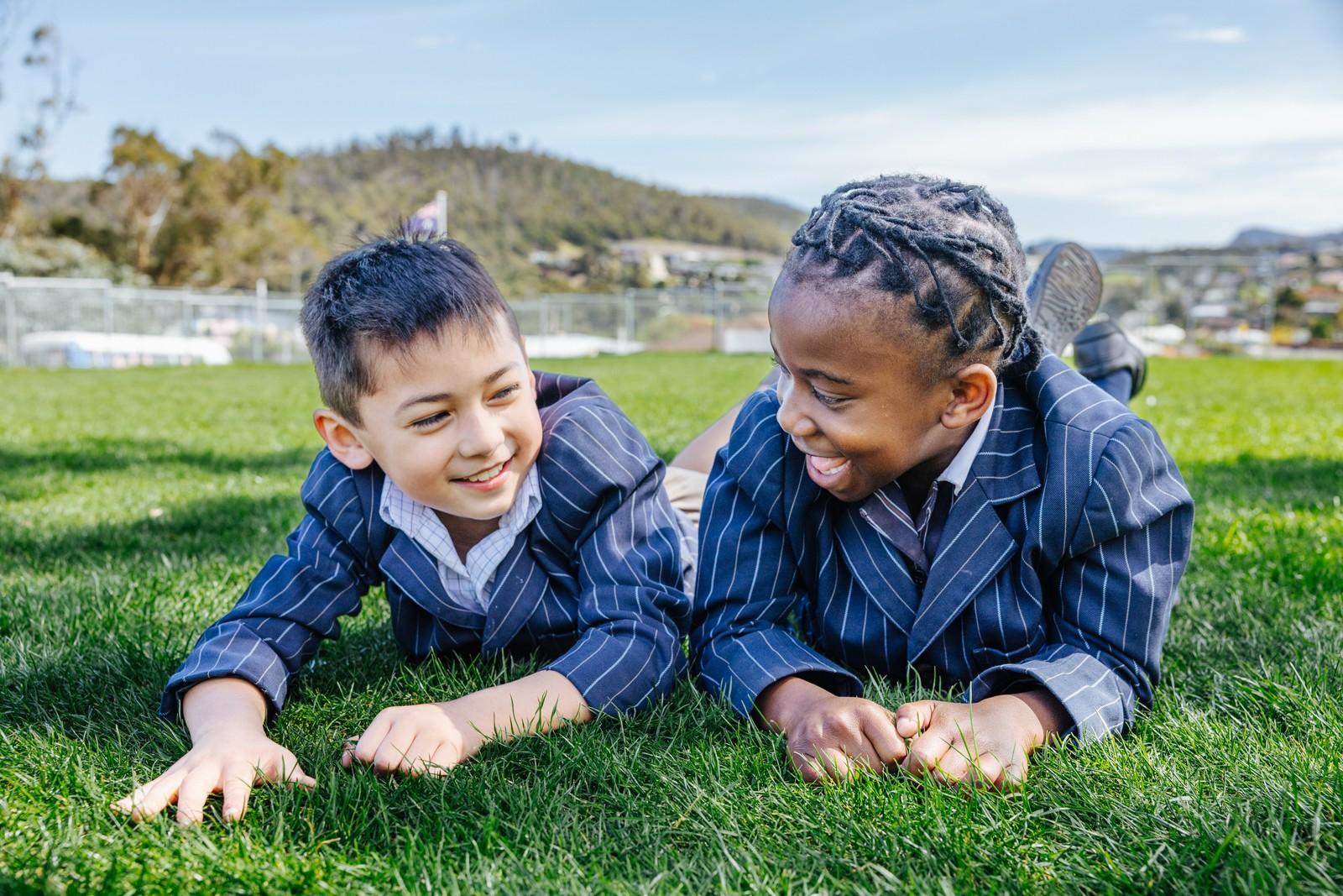 Two primary students lying on the grass, smiling at each other in Geilston Bay.