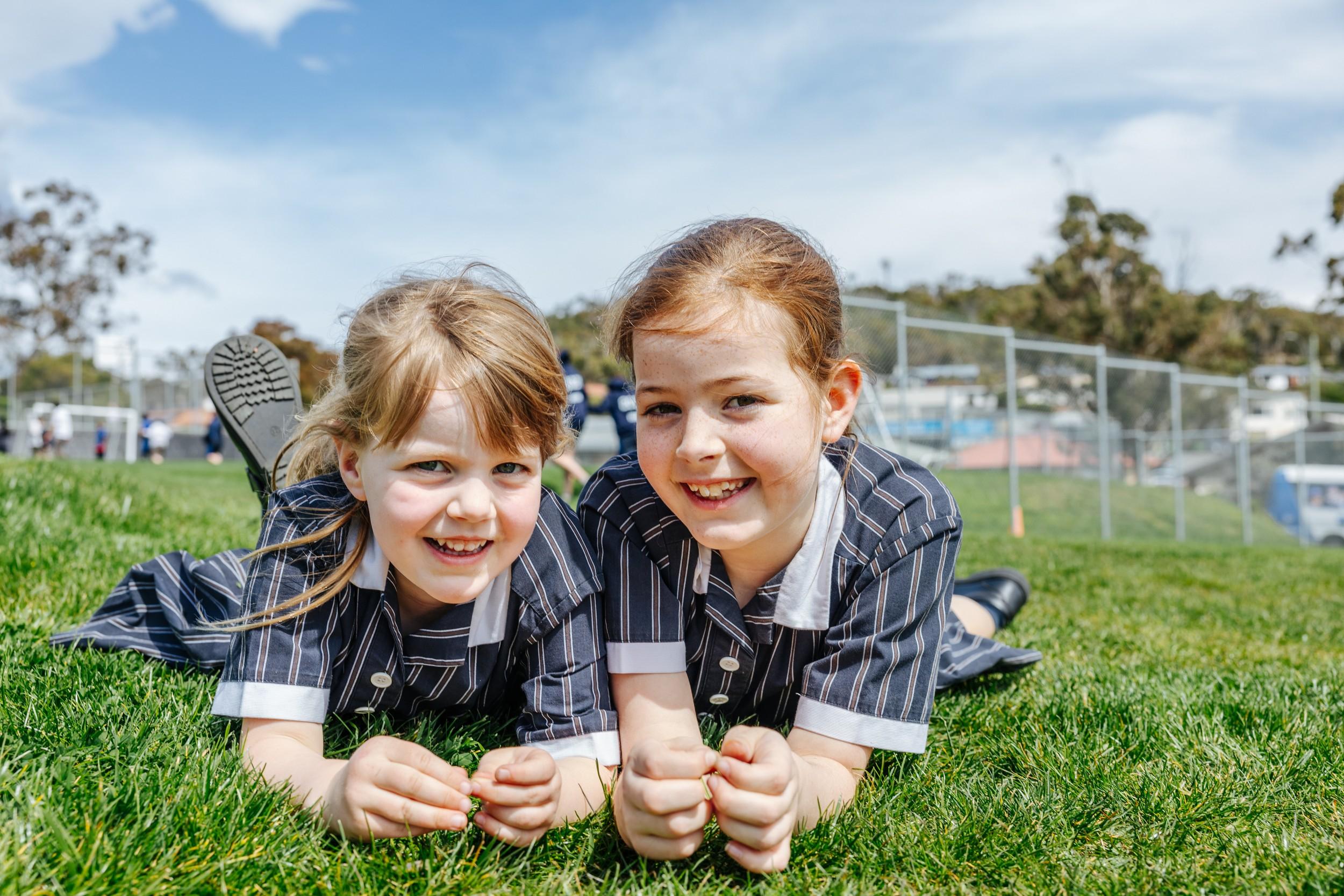 Primary students smiling together on the grass at ACC Hobart campus.