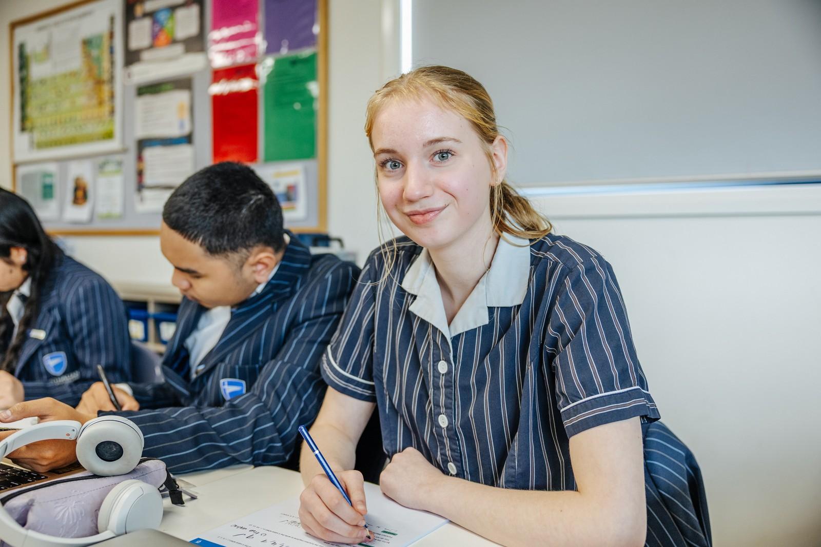 Secondary student writing at her desk in a classroom