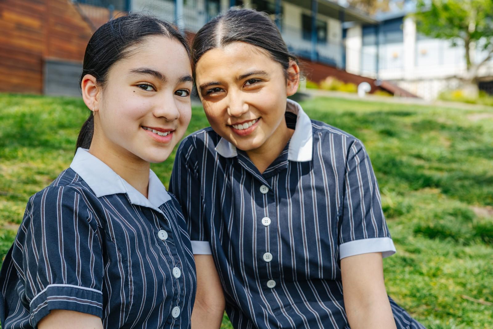 Two secondary students sit on the grass together, reflecting a caring school community