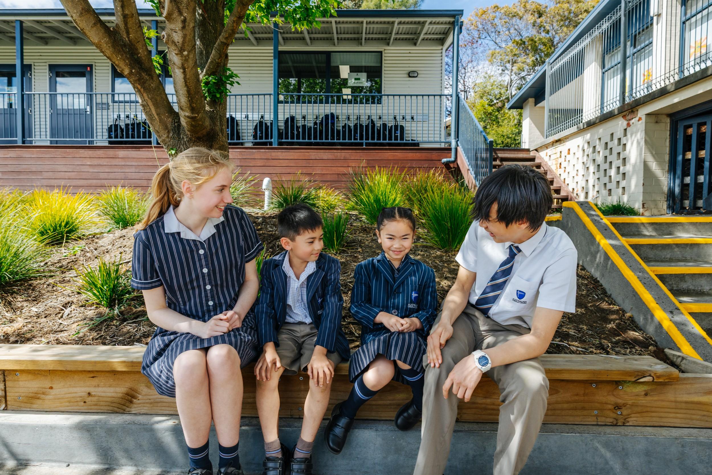 Students at ACC Hobart sit together on steps outside the Geilston Bay campus, chatting and smiling