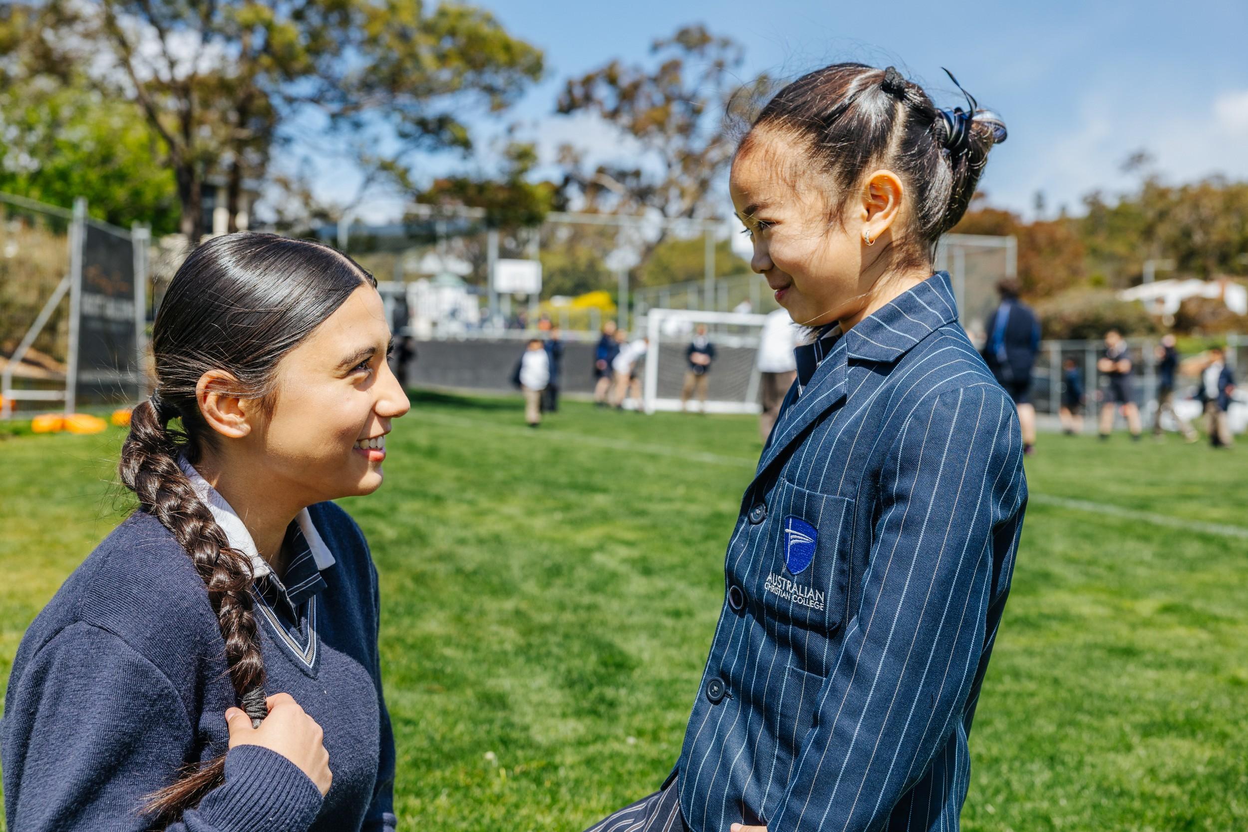 Two ACC Hobart secondary students smile warmly at each other on the school sports field