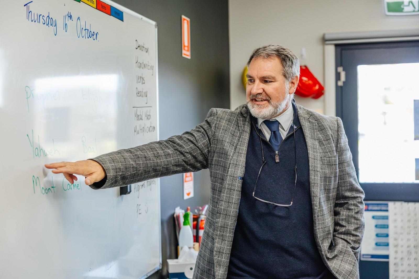 A teacher explains a lesson at the whiteboard during a structured classroom session