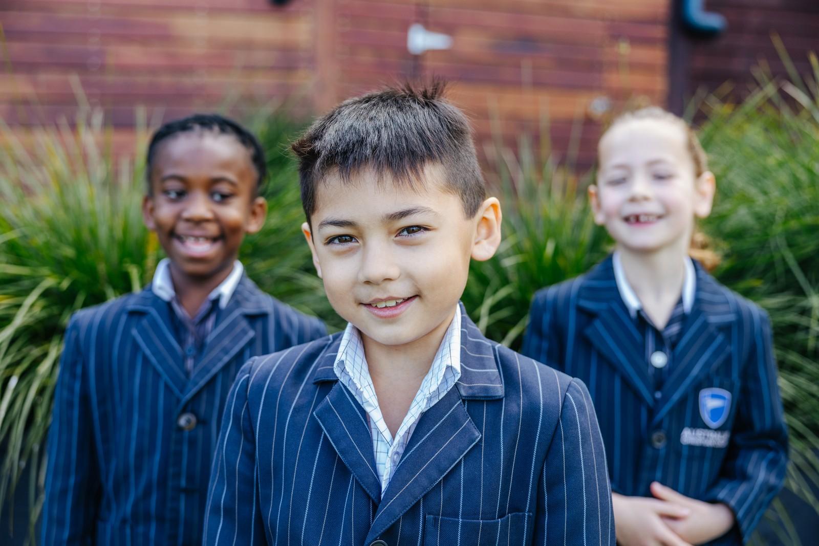 Three ACC Hobart Primary students in uniform smiling together outdoors.