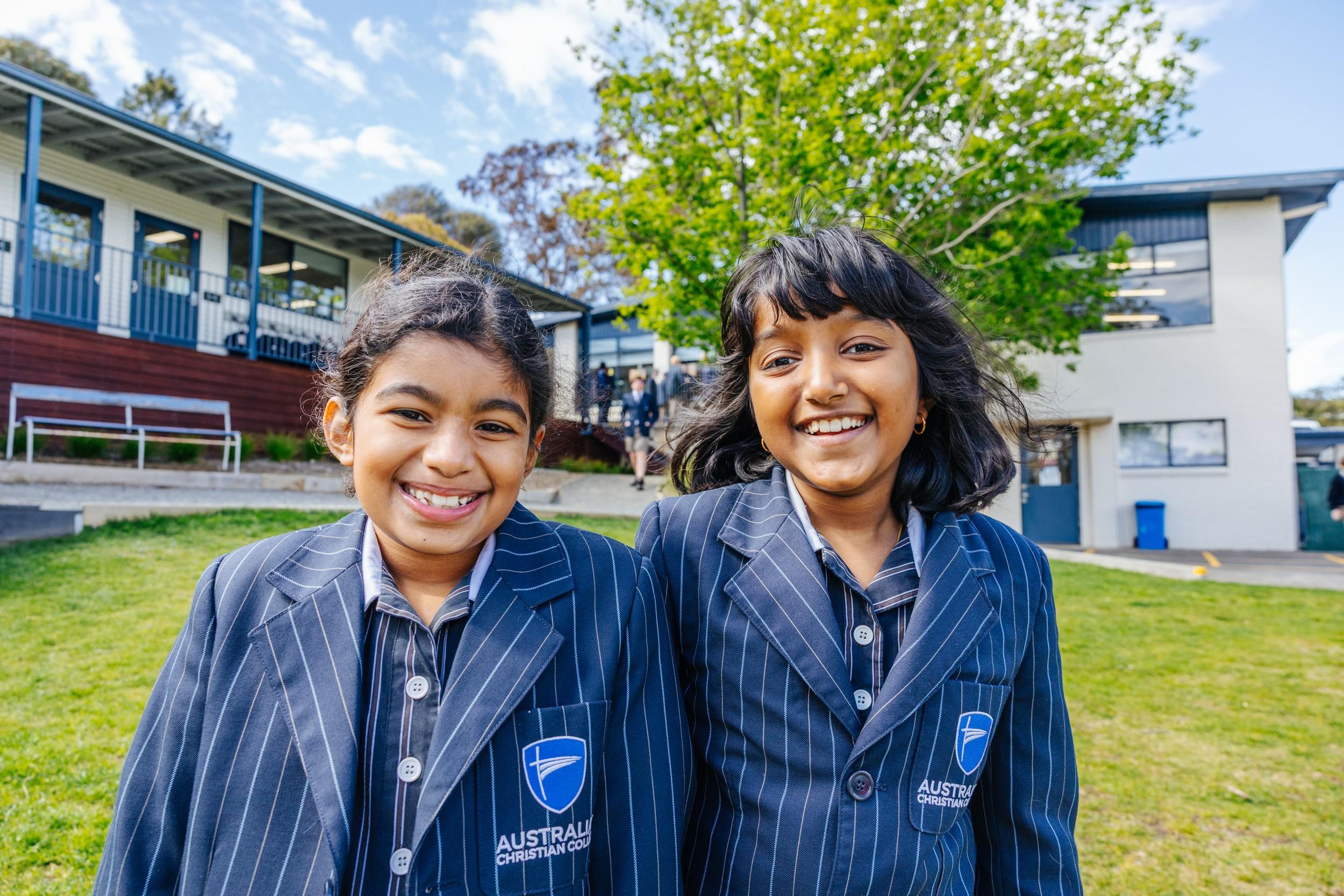 Two smiling ACC Hobart students in uniform standing together on campus, reflecting a close-knit school community.