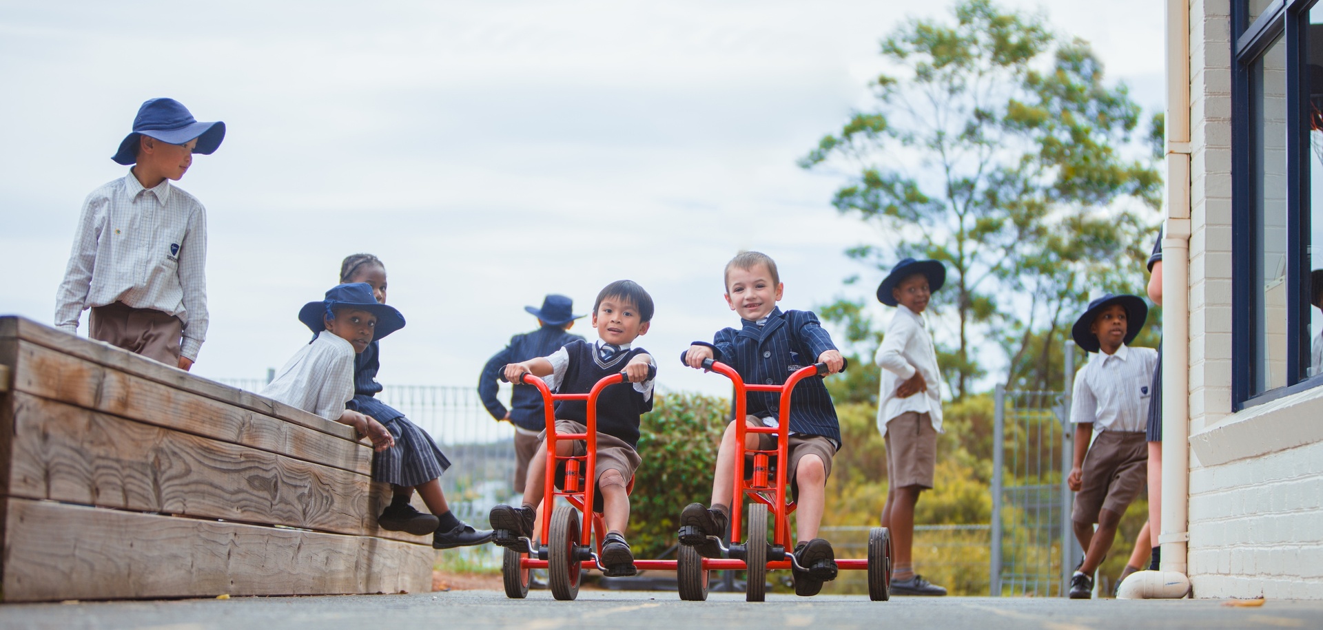 Primary school students in formal uniform riding tricycles around ACC Hobart campus
