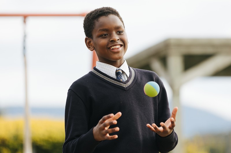 Male student wearing winter school uniform tossing a ball