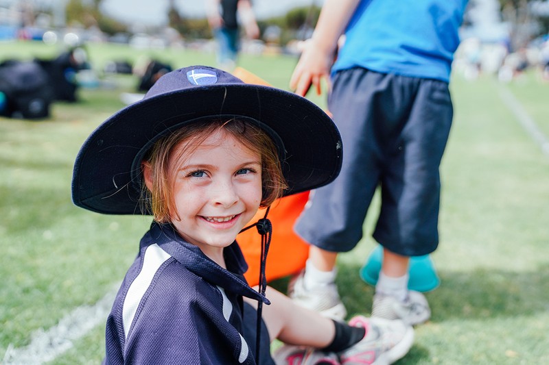 Primary aged girl sitting outside wearing ACC sports uniform and broadbrim hat