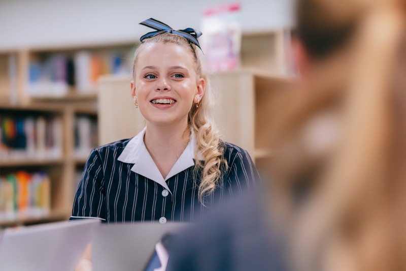 Smiling female student with hair-bow in library