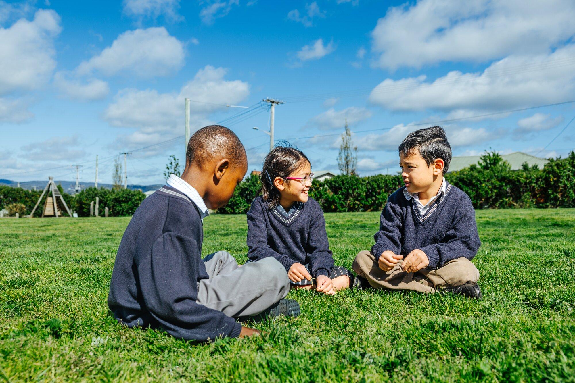 Primary students sitting and chatting together on the lawn at ACC Launceston