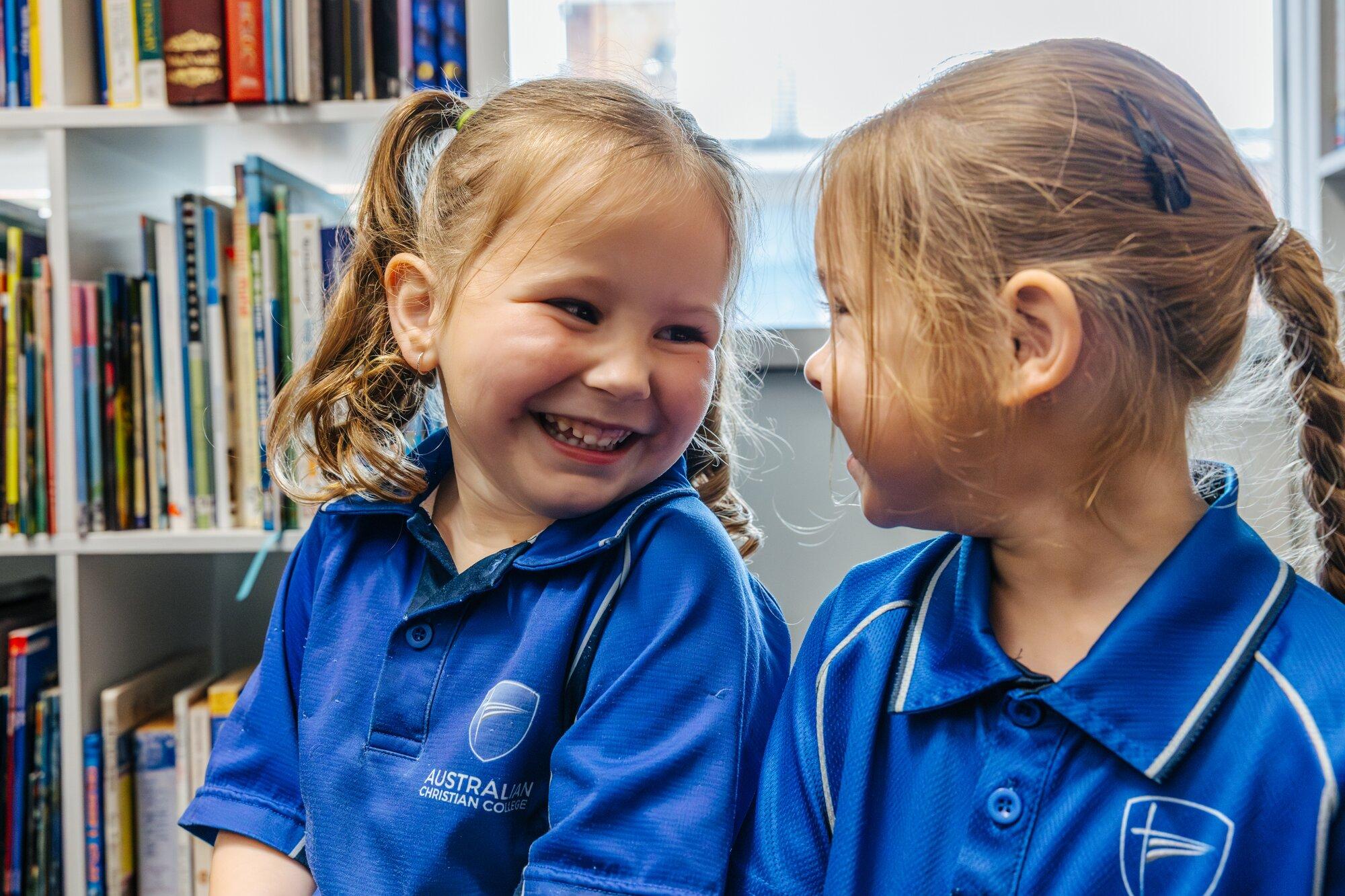 Two primary girls laughing together in the Newnham school library