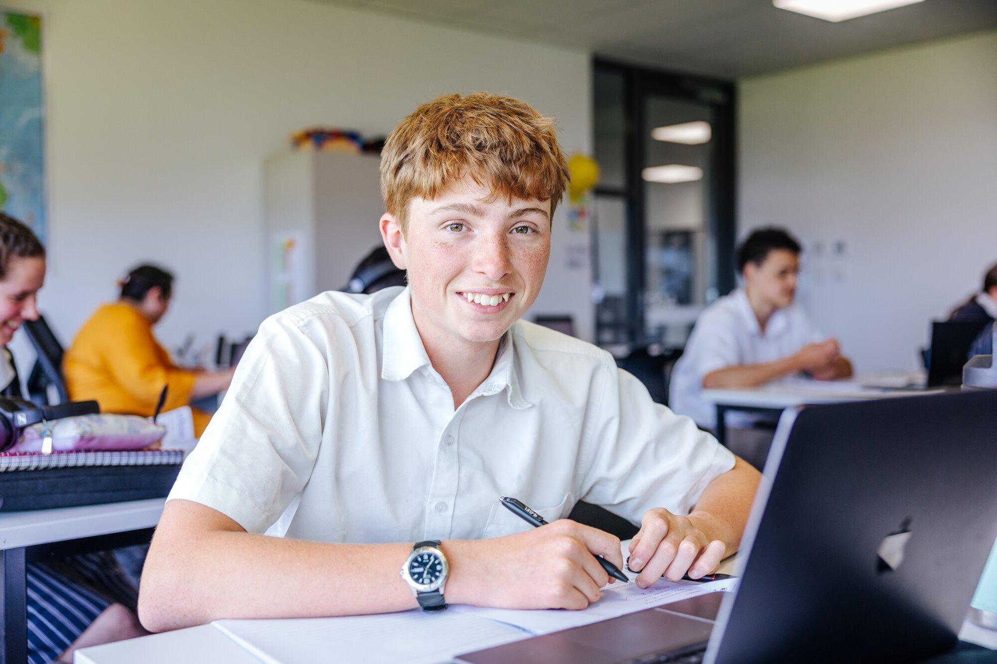 Secondary student smiling at a laptop in a Newnham classroom