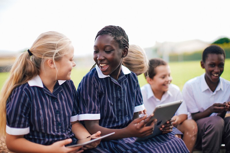Students holding ipads interacting with on another while sitting on a bench