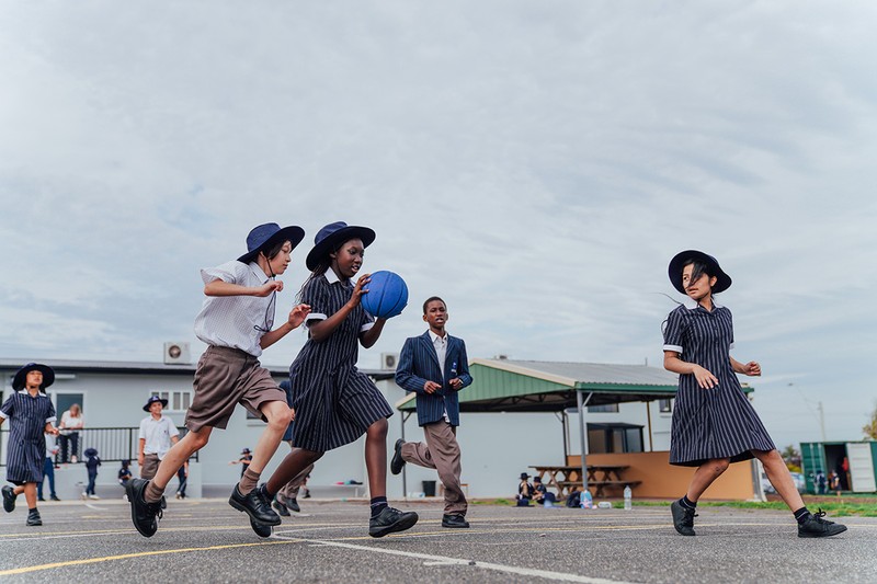 Group primary aged students in uniform playing with ball on court outside