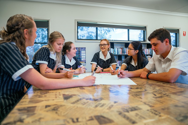 group of high school students sitting around table collaborating on group assignment