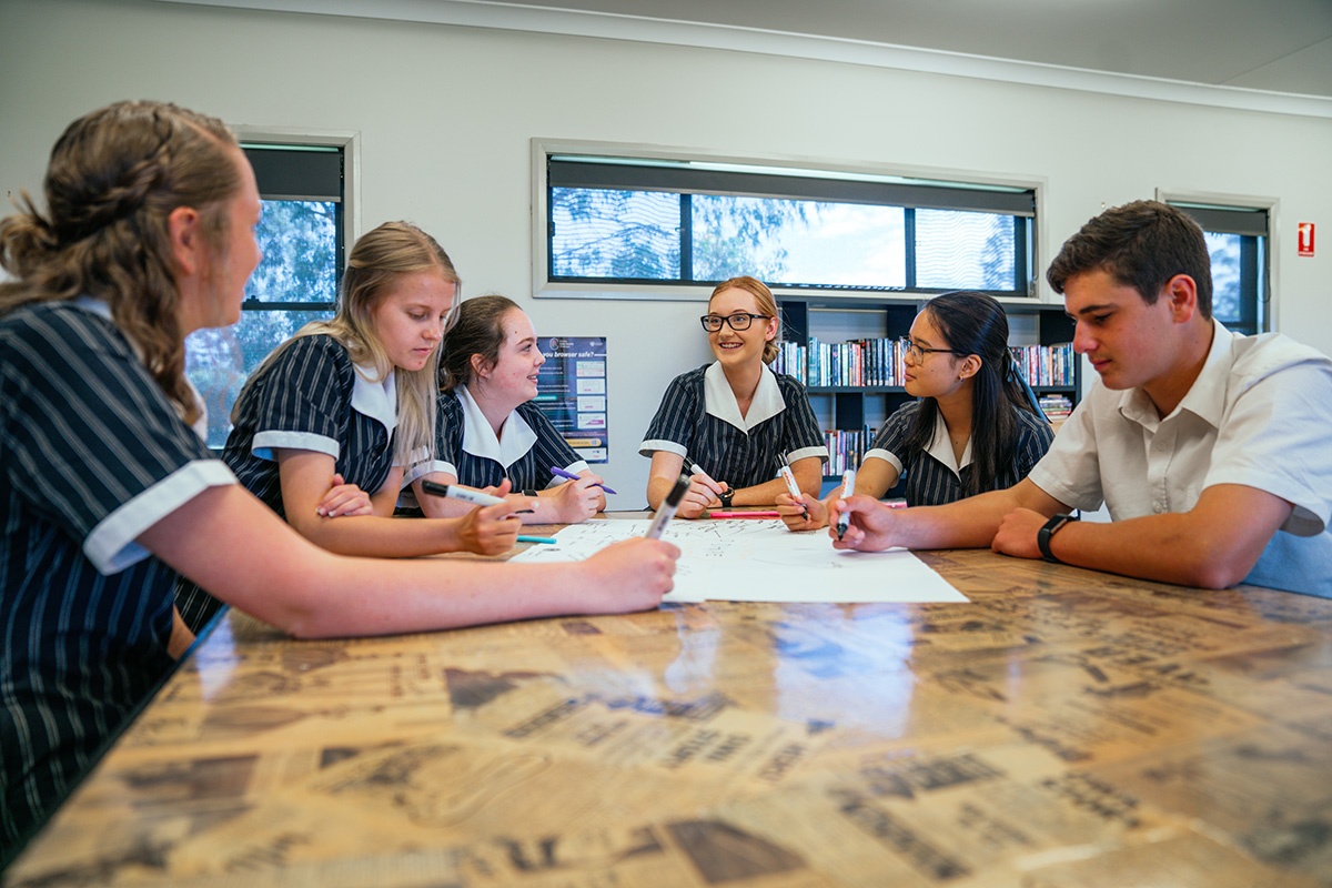 group of high school students sitting around table collaborating on large sheet of paper