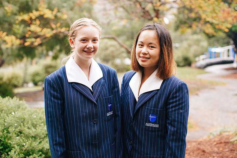 2 high school students wearing formal uniforms and smiling at the camera