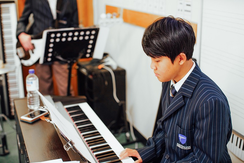 asian Launceston high school student wearing school uniform blazer playing keyboard in music class