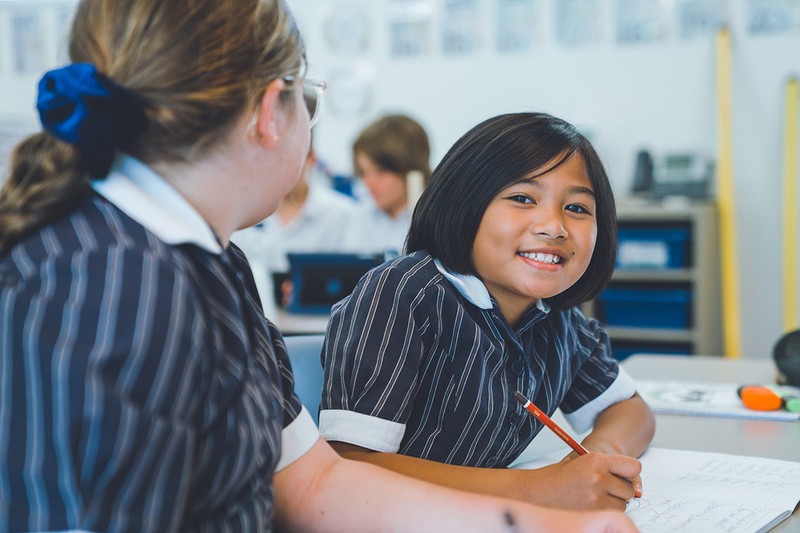 smiling ACC Launceston girl with bob haircut sitting at desk doing work holding pencil