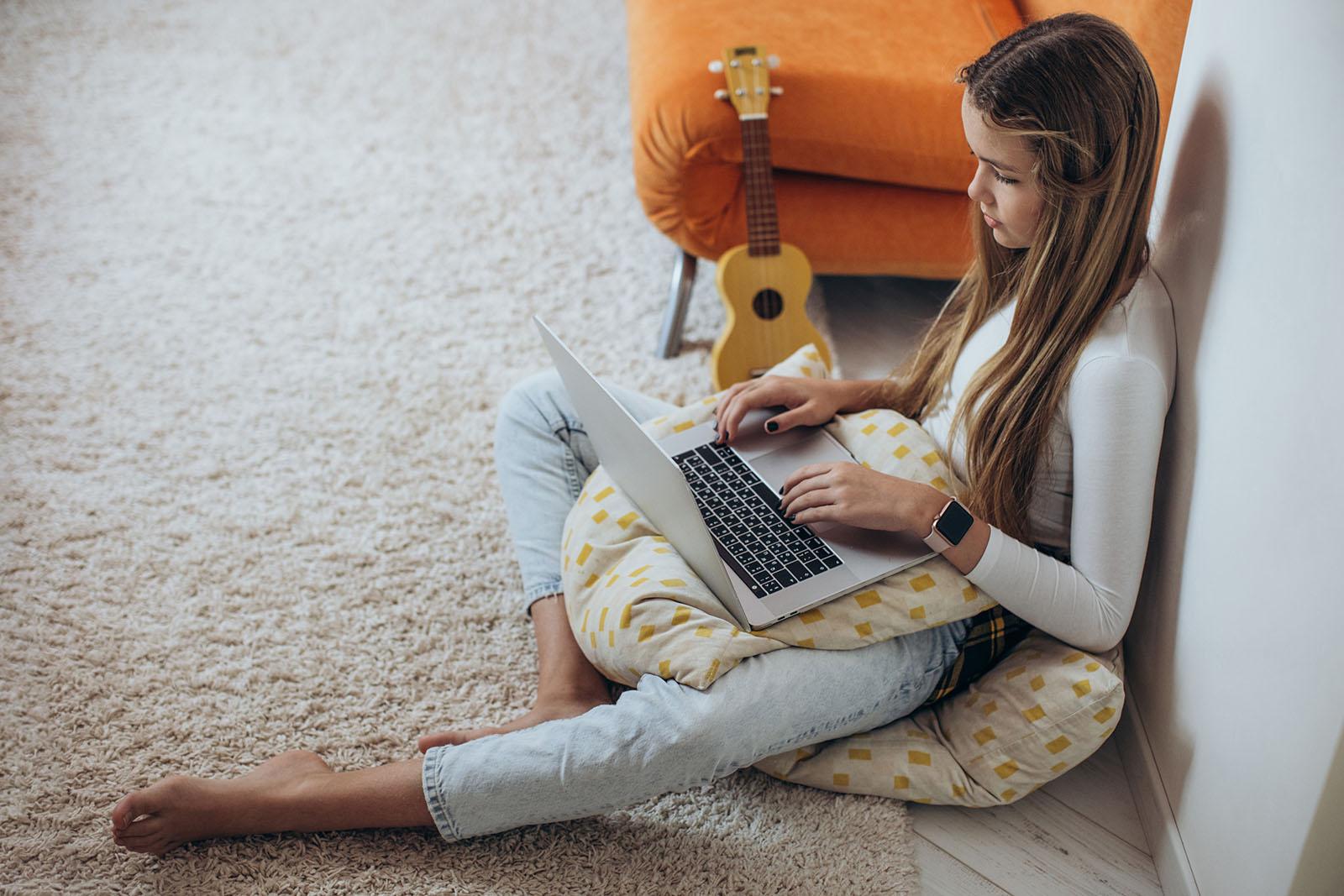 Student studying at home using a laptop while seated on the floor