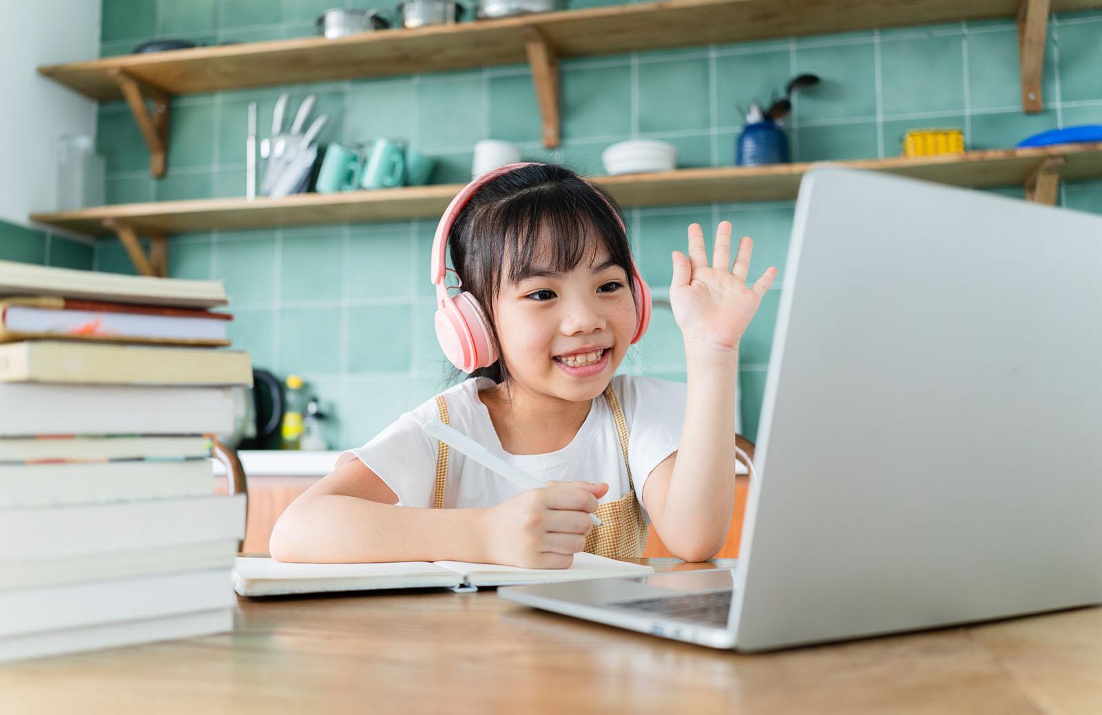 Student waving during a live online lesson from home