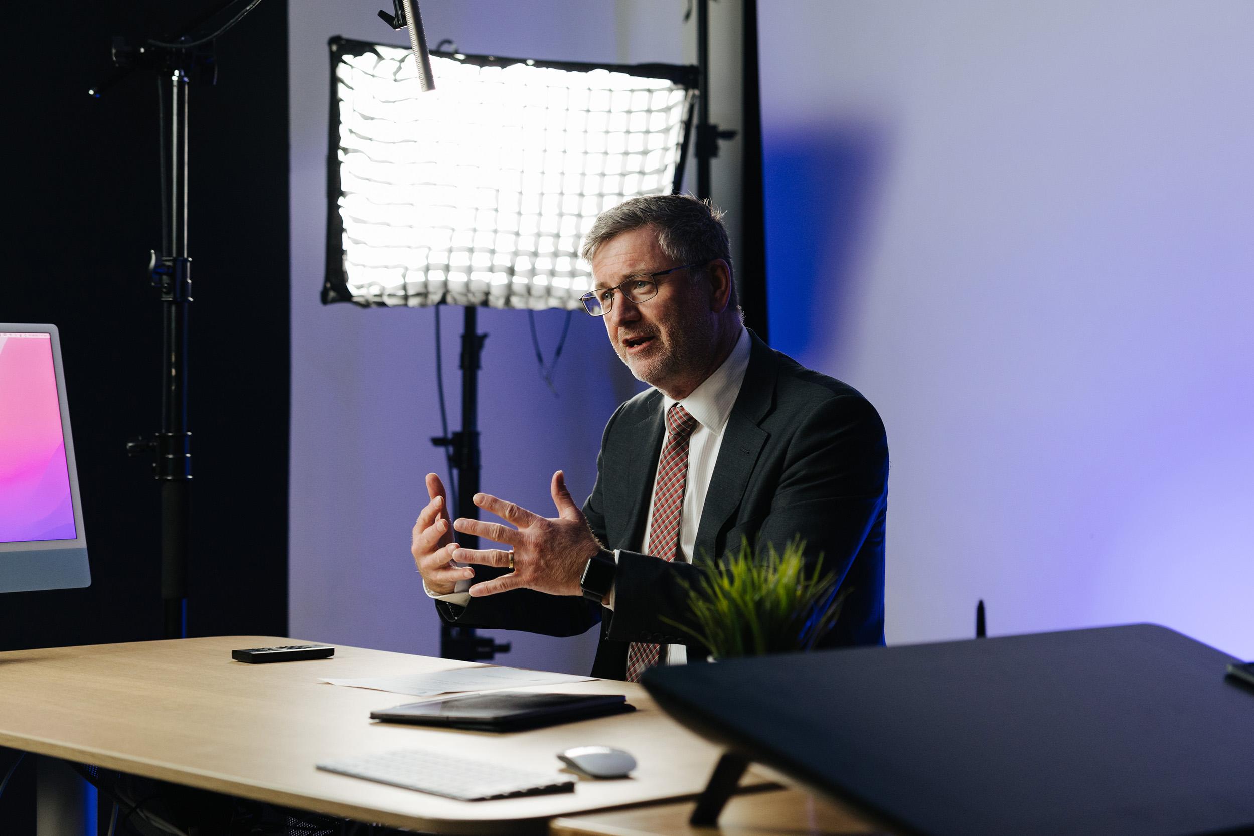 Principal engaged in thoughtful conversation in front of studio lights